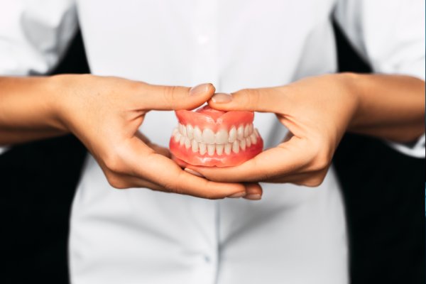 Dentures in Stuart — hand holding a full set of dentures with pink gums and white teeth